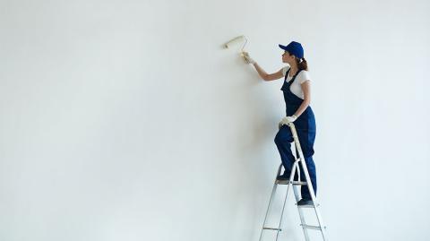 Femme qui peint un mur depuis une échelle